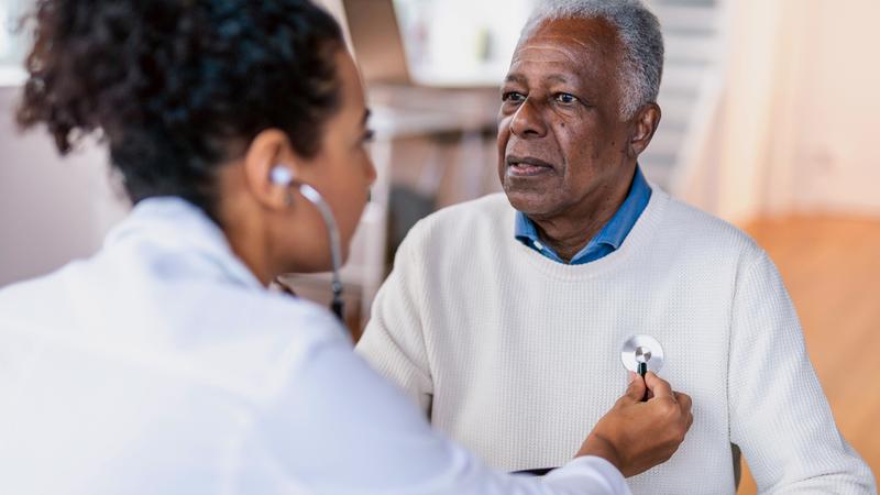 A doctor listens to the heart of a senior male patient.