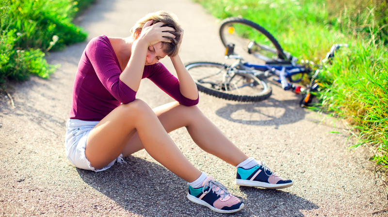 A woman sits on the ground and holds her head after falling off of her bicycle.