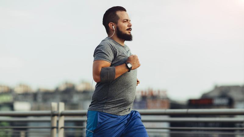 A middle-aged man runs in an urban setting while listening to music.