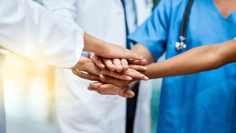 Healthcare workers stand together with hands stacked on top of one another.