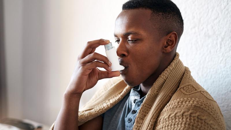 A young man sitting alone in his bedroom and using an asthma pump.