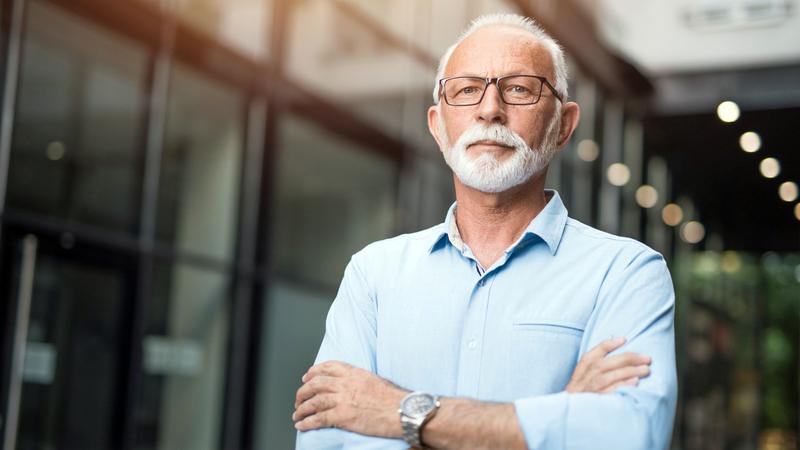 Senior businessman with arms crossed looking at camera.