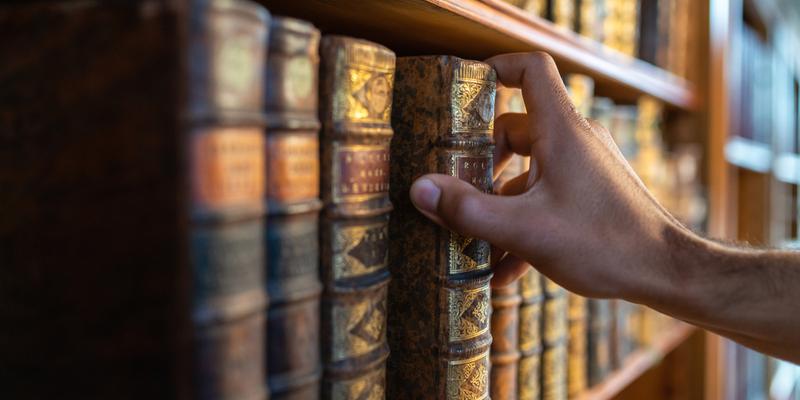 A close-up photo of a hand taking a medical publication book off of a bookshelf in a library.