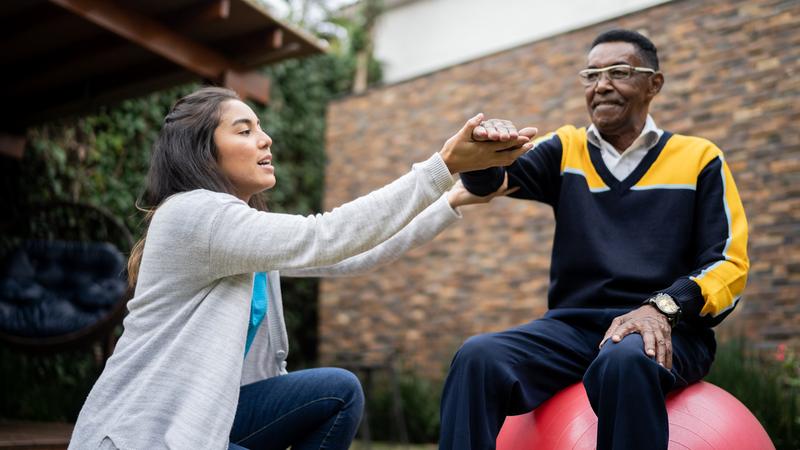 Senior man doing exercise lifting arms with physical therapist at home