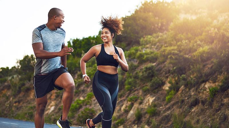 A young african american couple smiles as they run together outdoors.