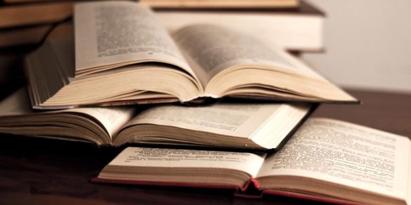 A pile of open books sit stacked on a table.