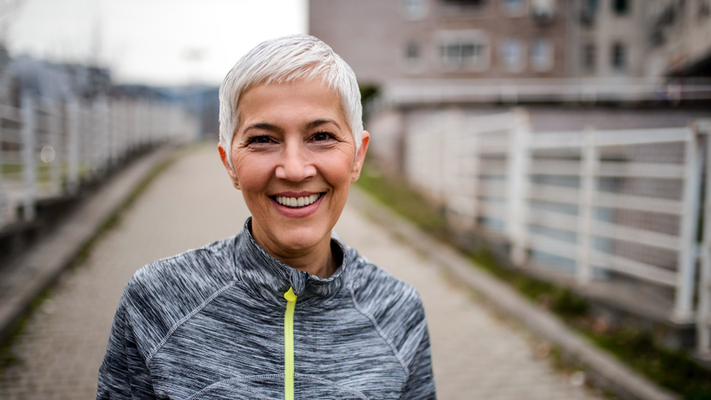Portrait of a sporty smiling senior mature woman wearing athletic clothing, standing outdoors.