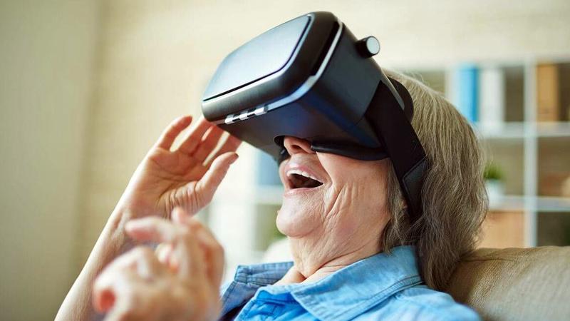 A senior woman laughs with delight while wearing a virtual reality headset.