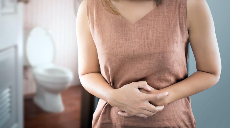 Close up of a woman clutching her stomach in pain. A bathroom is out of focus in the background.