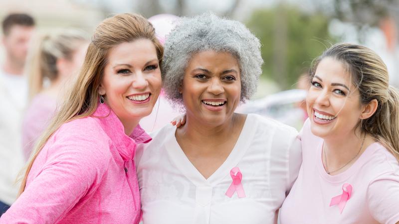 Beautiful diverse women enjoy attending breast cancer awareness event together. They are wearing pink clothing with breast cancer awareness ribbons.