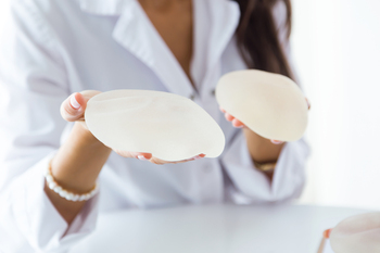 A doctor holds a pair of breast implants in a clinical setting.