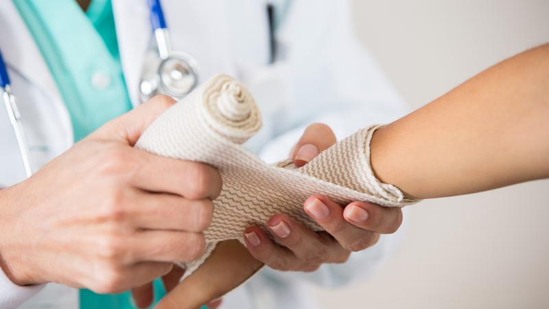 Close up photo of a medical professional wrapping a person's wrist with a bandage.