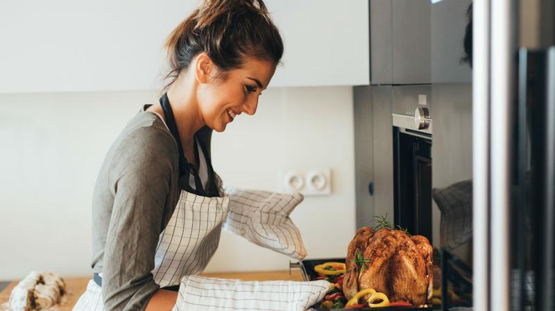 A woman bastes a turkey in her home kitchen.