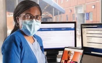 一名MedStar Health服务人员在几台电脑前合影，其中一台电脑是与一名打电话来进行远程医疗访问的女性患者合影的。