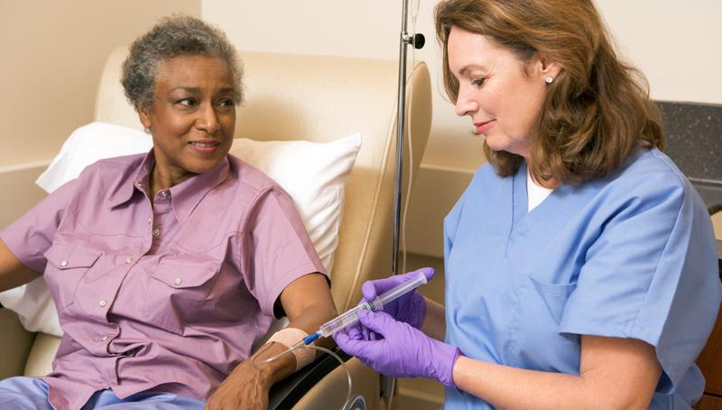 A nurse gives intravenous medications to a patient who is seated.