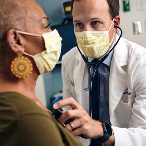 Dr Brian Case listens to the heart of a patient during an office visit at MedStar Health. Both people are wearing masks.