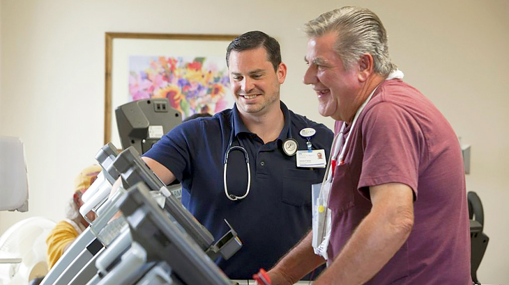 A physical therapist talks with his patient who is walking on a treadmill during a physical therapy session.