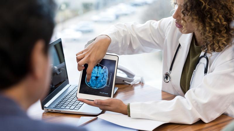 A doctor points to an ipad which shows a brain scan while discussing a diagnosis with a patient.