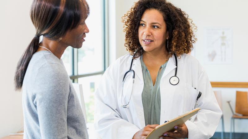 A female patient and her doctor stand together as they discuss the test results on the clipboard held by the doctor.