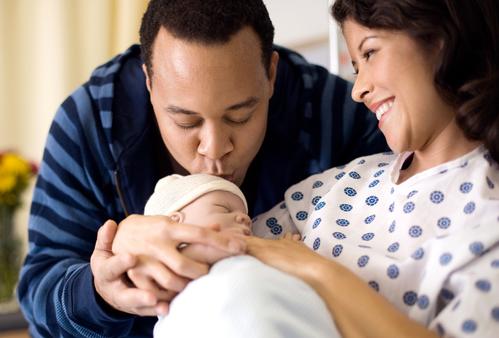 A mother holds her newborn baby while the father kisses the baby's forehead.