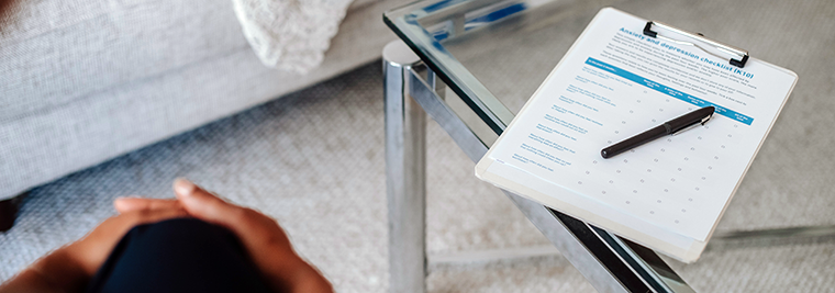 A clip board and pen with a medical form sits on a glass-top table.