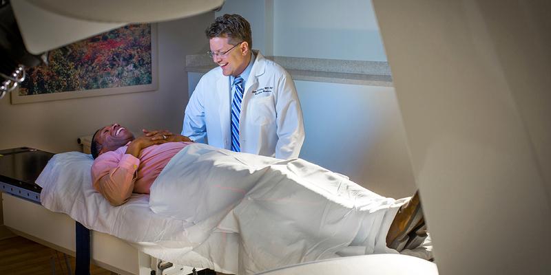 Dr Sean Collins talks with a patient who is laying on the bed of the cyberknife at MedStar Georgetown University Hospital.