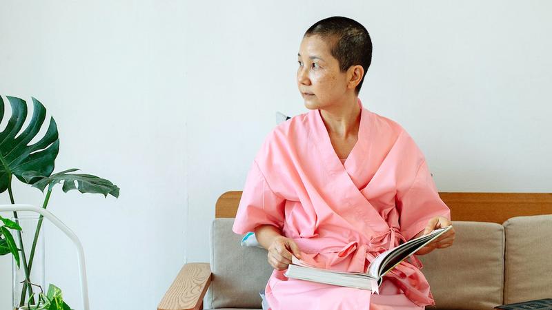A female patient, wearing a pink robe, sits in a waiting room and reads a magazine.