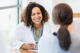 一位中年女医生微笑着听一位女病人谈论她的健康状况。