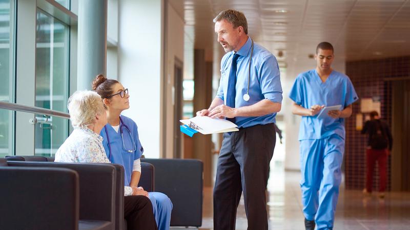 Healthcare professionals talk with a patient in a hospital lobby.