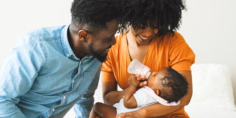 A mother and father bottle feed their newborn baby.