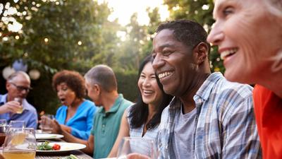 A diverse group of adults joyfully share a meal together outdoors.