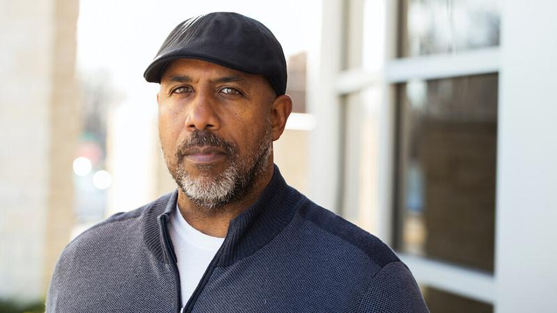 An older African American man wearing a grey hat looks at the camera.