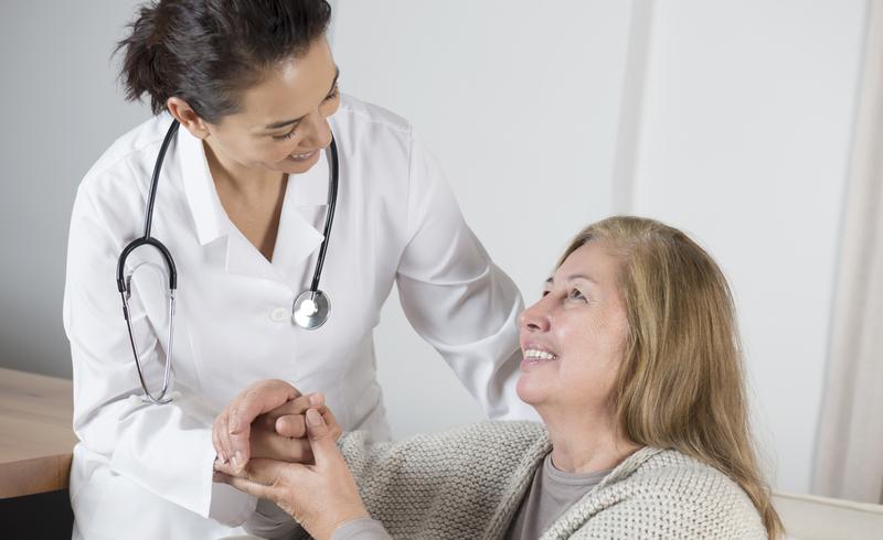 A female doctor comforts an older female patient in a clinical setting.