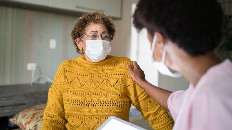 A doctor consoles a senior patient in a hospital room - wearing facial mask