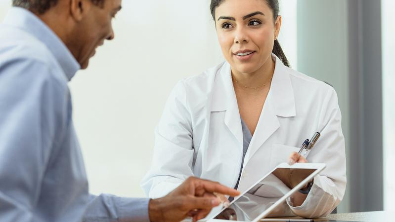 A female provider talks with an older male patient and shows him something on the ipad.