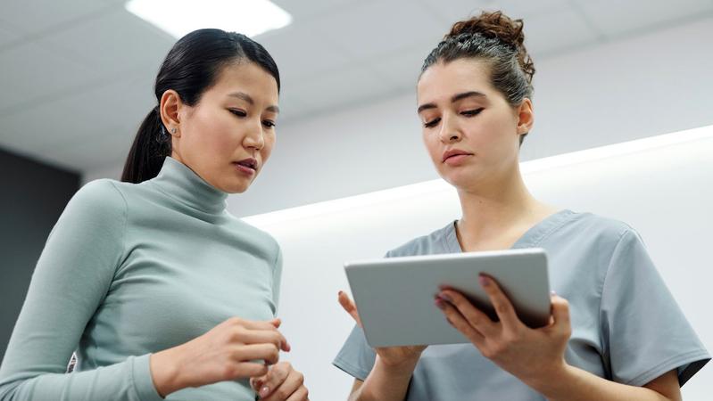 A nurse talks with a patient while showing her information on an ipad.