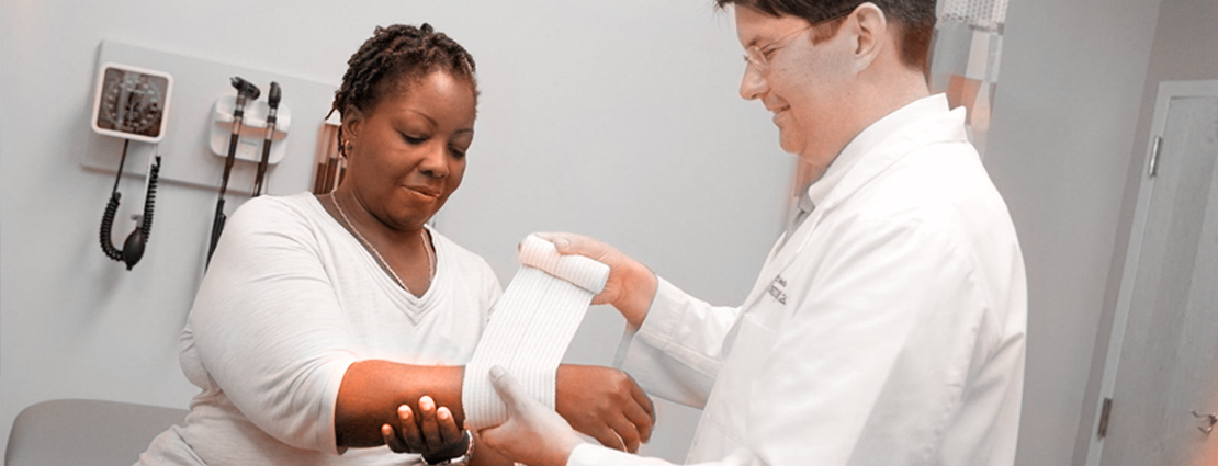 A doctor applies a bandage to a female patient's wrist in a clincial setting.