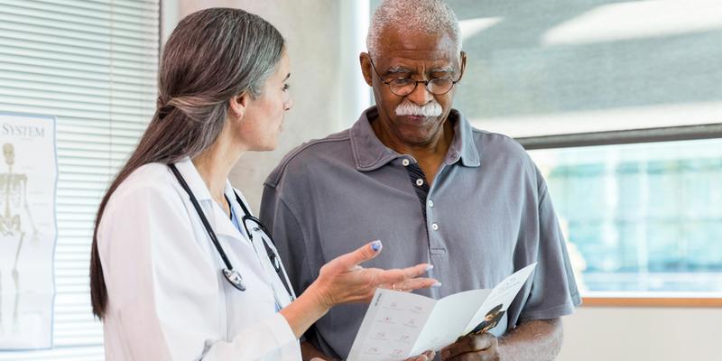 A doctor talks with a mature African American male patient in a clinical setting.