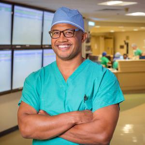 Dr Wiemi Douoguih stands with arms crossed and smiles while standing in a hospital hallway.