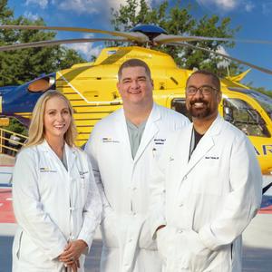 Doctors Taryn Travis, Jeffrey Shupp and Shawn Tejiram pose for a photo on the helipad at MedStar Washington Hospital Center. The helicopter is in the background.