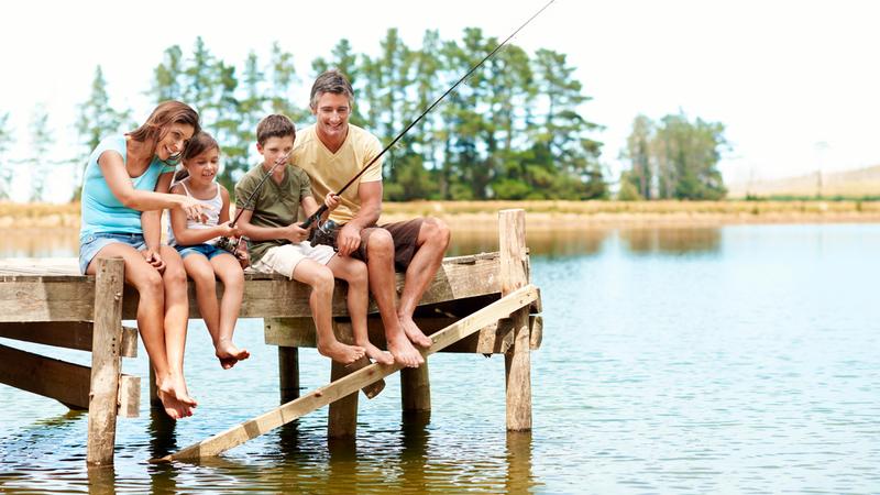 A family of four fishing together while sitting on a pier at a lake.