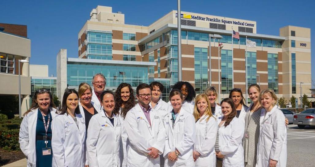 The faculty of the Family Medicine Residency program poses for a photo outside with MedStar Franklin Square hospital in the background