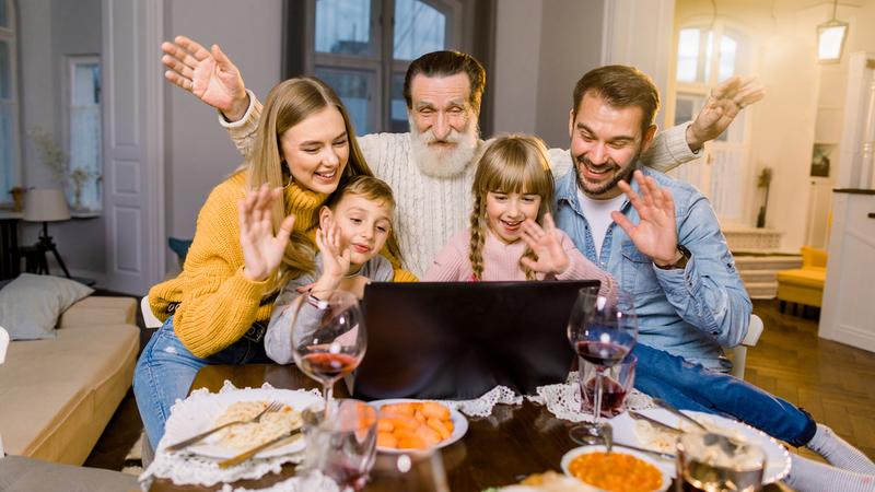 Beautiful family, sitting at the table with dinner meal, smiling, happy and using laptop. Family making videocall using laptop celebrating at home.