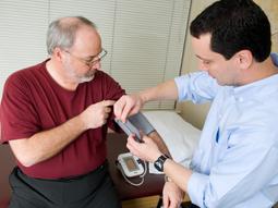 在临床环境中，医生为一位老年男性患者测量血压。这张照片是从高角度拍摄的。