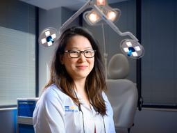 Dr Ming Deng poses for a photo with dramatic lighting in front of the patient examining table in her dermatology office.