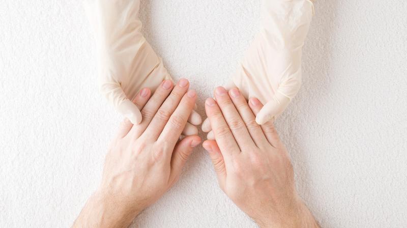 Close up photo of a doctor's gloved hands holding a patient's hands.