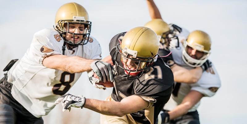 Close up photo of three football players wearing gold helmets playing in a game.