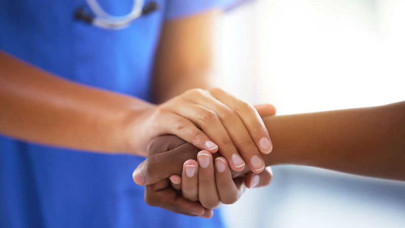 Close up photo of a nurse holding the hand of a patient.