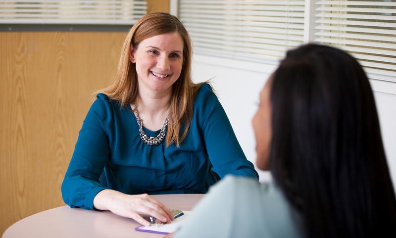 Emily Kuchinsky sits at a table and talks with a patient about genetic counseling.