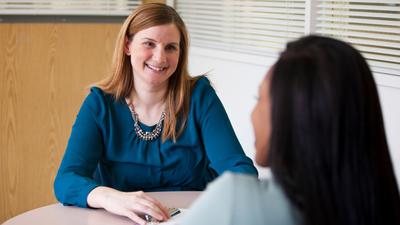 Emily Kuchinsky sits at a table and talks with a patient about genetic counseling.